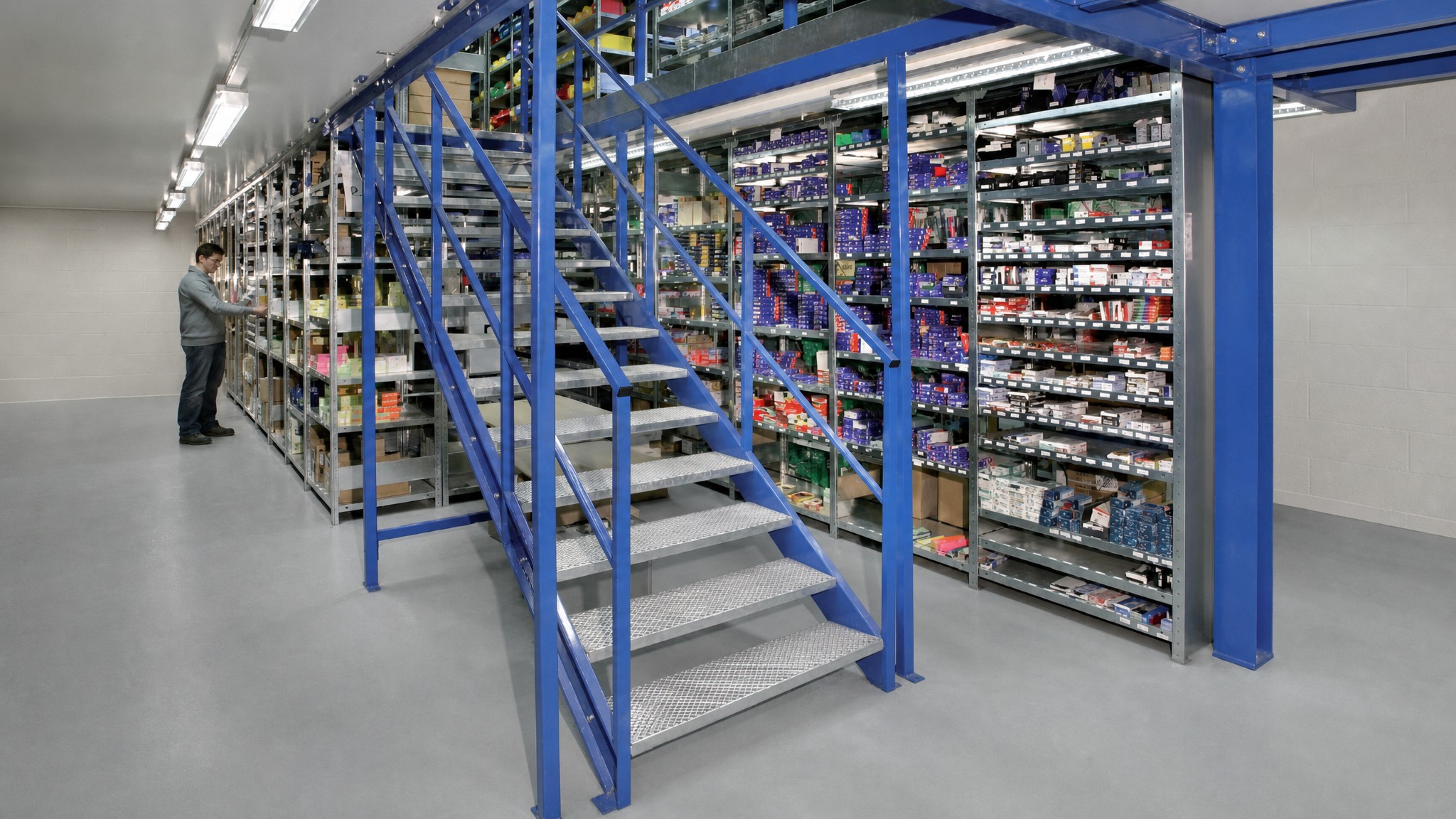 A multi-level catwalk racking system with stair access and shelving holding small parts in an industrial setting.