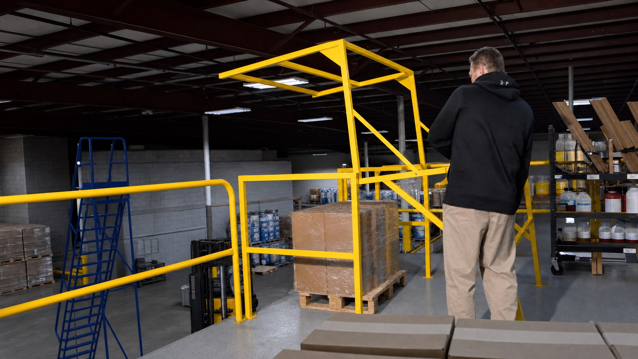 Person standing by a yellow mezzanine safety gate next to a pallet on an elevated platform.