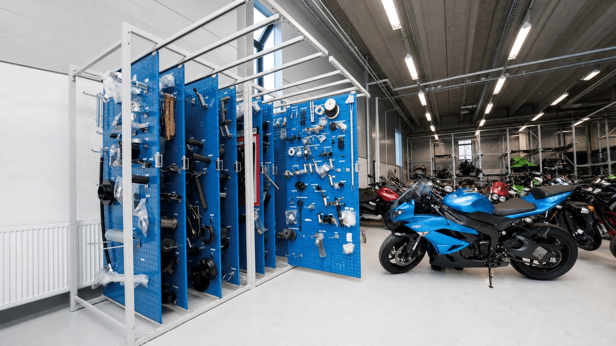 Sliding blue pegboard racks holding assorted tools and parts in a workshop with motorcycles.