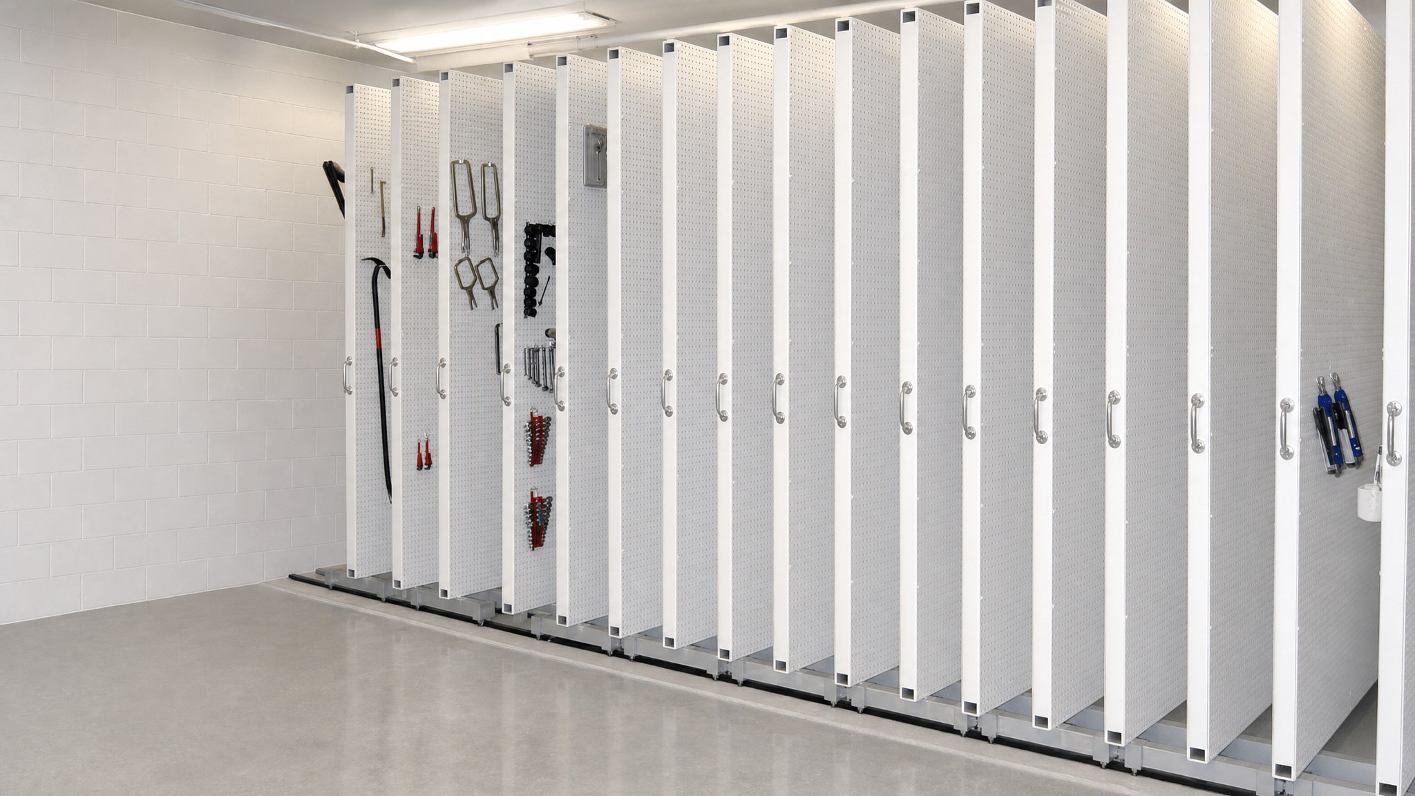 Row of sliding white pegboard panels with various tools hanging on hooks.